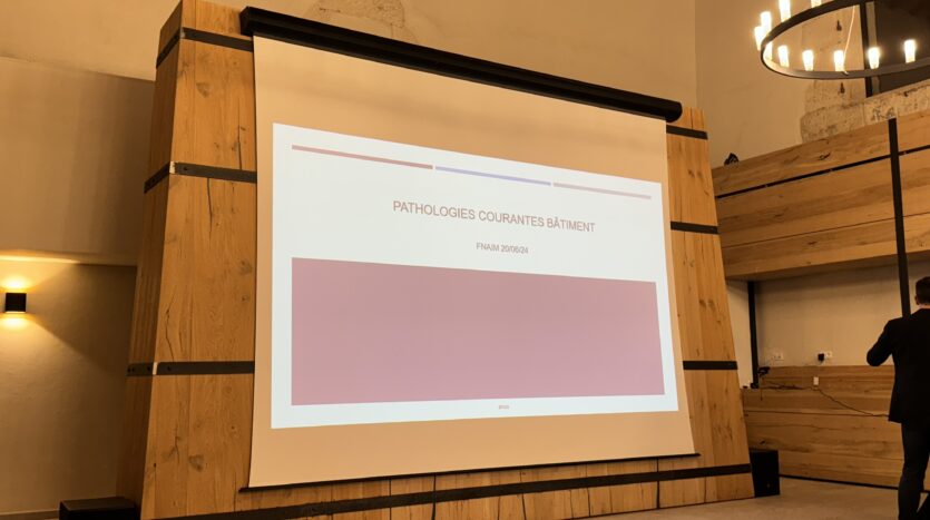 Présentation sur les pathologies courantes du bâtiment, homme debout près de l'écran.