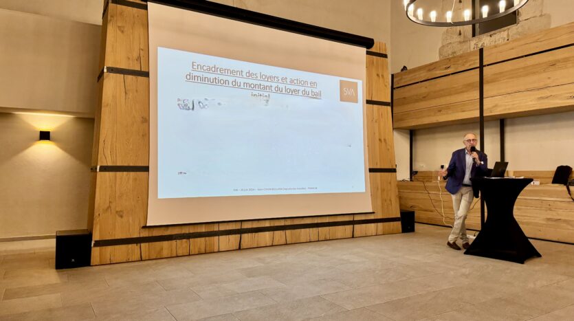 Personne exposant sur l'encadrement et la réduction des loyers, diapositive projetée en salle.