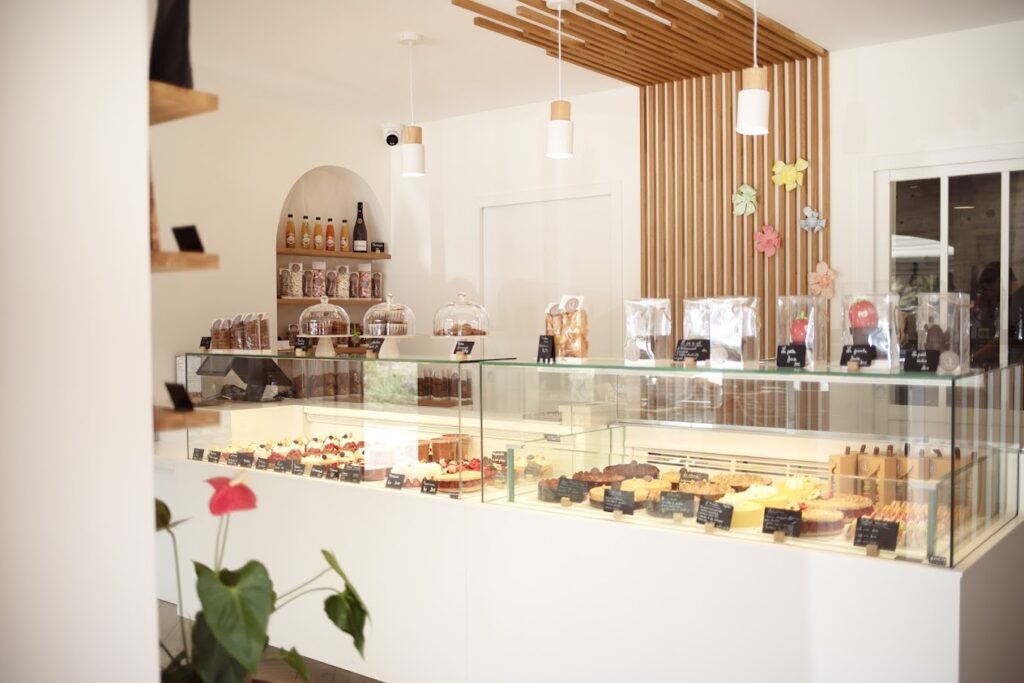 Pâtisserie moderne avec présentoir de desserts et produits emballés, décor bois et luminaires.