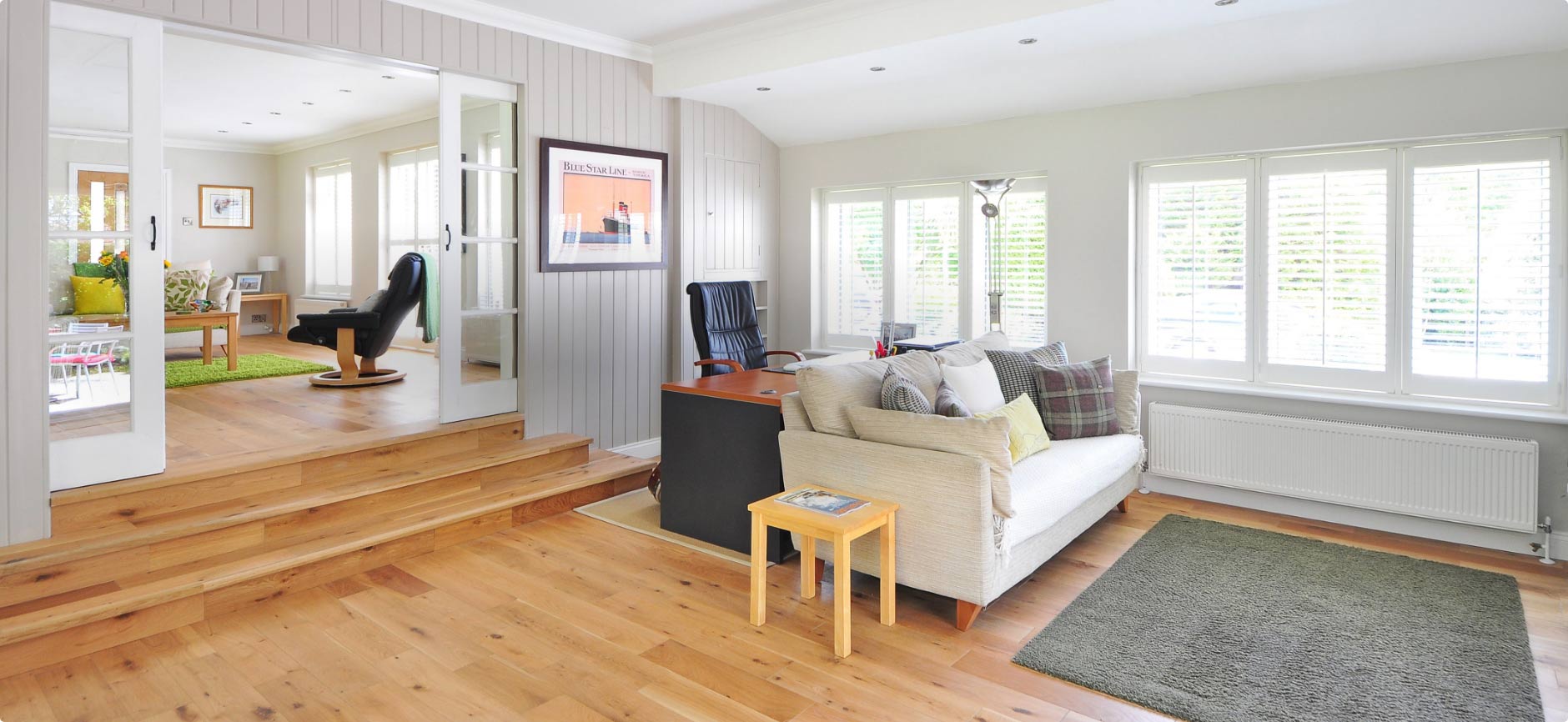 Luminosité et modernité avec parquet, canapé, bureau noir et espace surélevé décoratif.