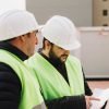 Trabajadores de construcción revisando planos con cascos y chalecos de seguridad en obra en construc.