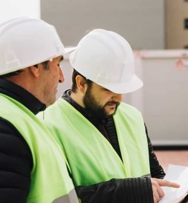 Trabajadores de construcción revisando planos con cascos y chalecos de seguridad en obra en construc.