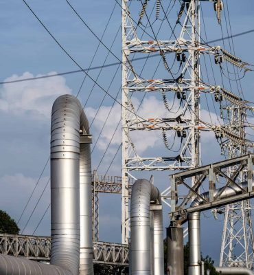 Torre de transmisión eléctrica con cables de alta tensión y tuberías metálicas en una planta industr.