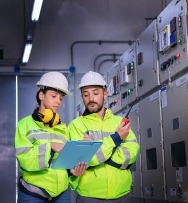 Técnicos revisando paneles eléctricos en planta industrial con equipo de protección.