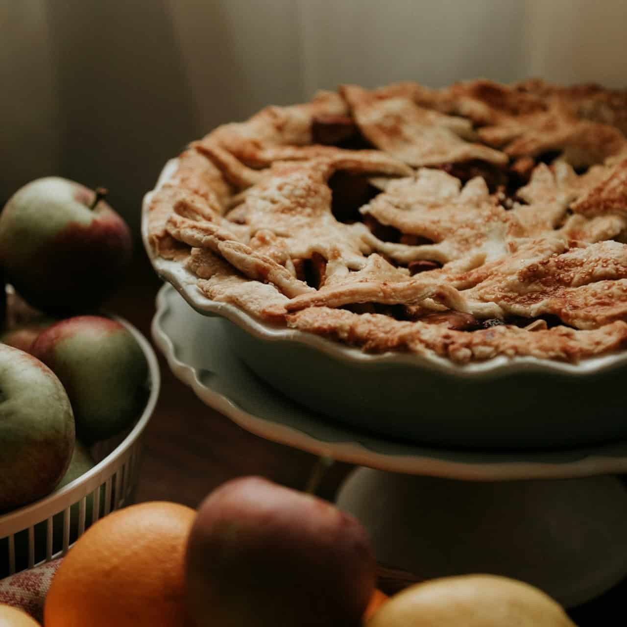 Appeltaart bakken? Een foto van een mooie appeltaart met appels op de achtergrond.