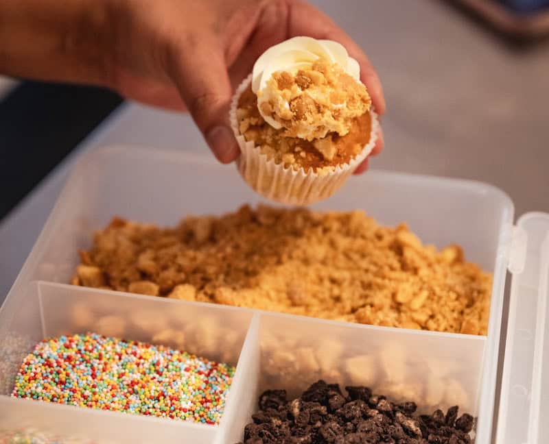 Een foto van een hand die bezig ermee is een cupcake te versieren.