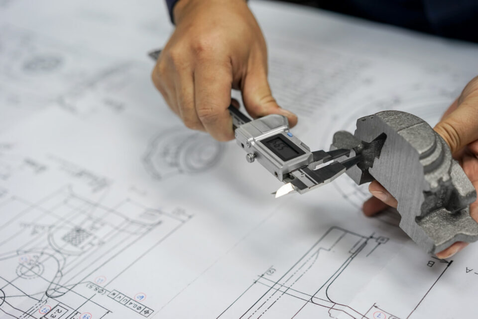 Close-up view of an industrial drawing with a hand holding a caliper while measuring a wear part.