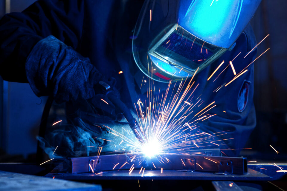 Welder with welding helmet welding a part.