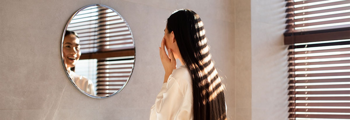 Vrouw die zich wast met hotel douchegel en shampoo, spiegel en raam op achtergrond.