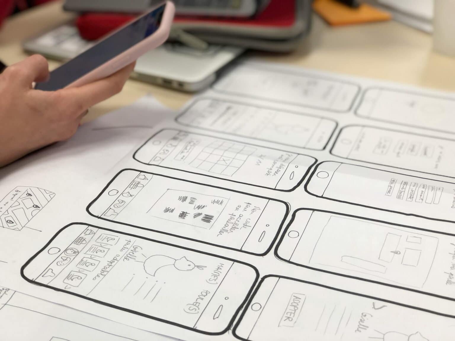 UX designer sketches app wireframes on paper, phone in hand.