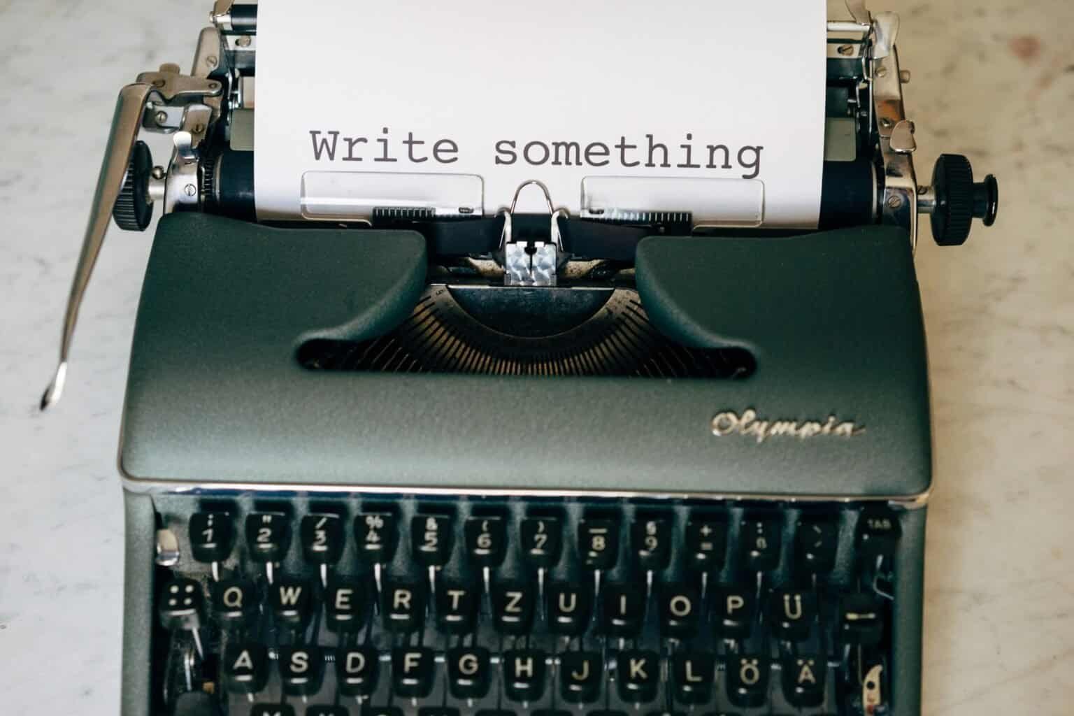 Vintage Olympia typewriter with "Write something" typed on paper.