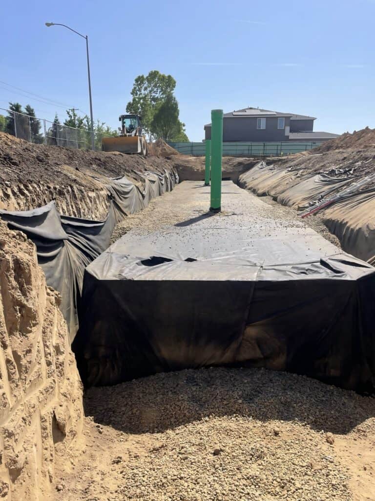 Geocellular module installation showing workers assembling modular crate units in excavated trench with geotextile wrapping