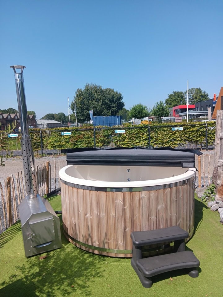 Houten hot tub in tuin met blauwe lucht.