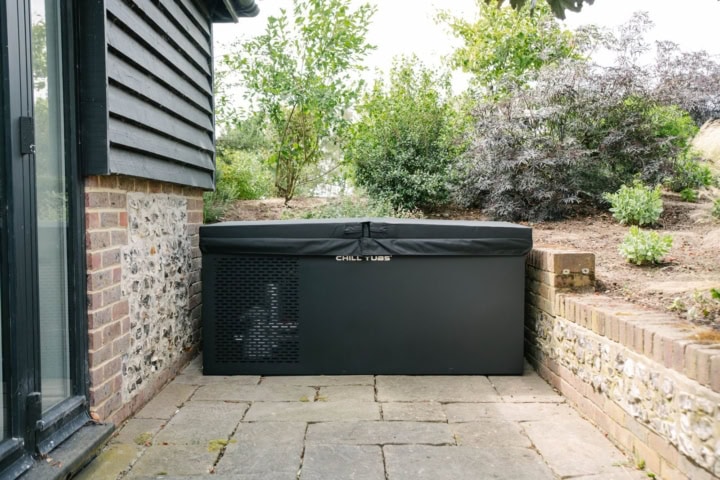 Zwarte buitenkoeling naast bakstenen muur en planten.
