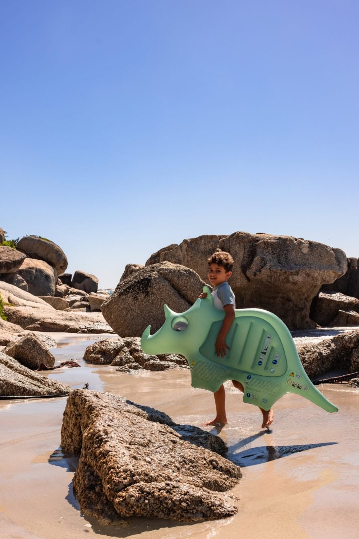 Kind speelt met dinosaurusspeelgoed op rotsachtige kust.