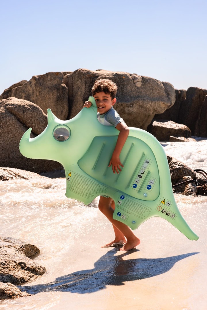 Kind met dinosaurus luchtbed op het strand.