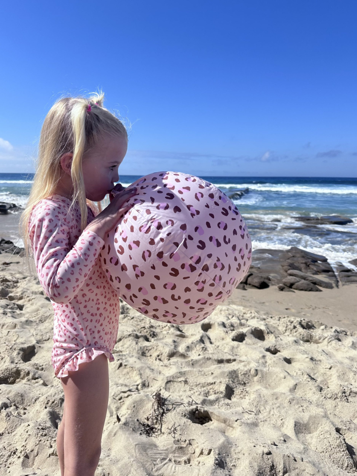Meisje blaast roze bal op aan strand.