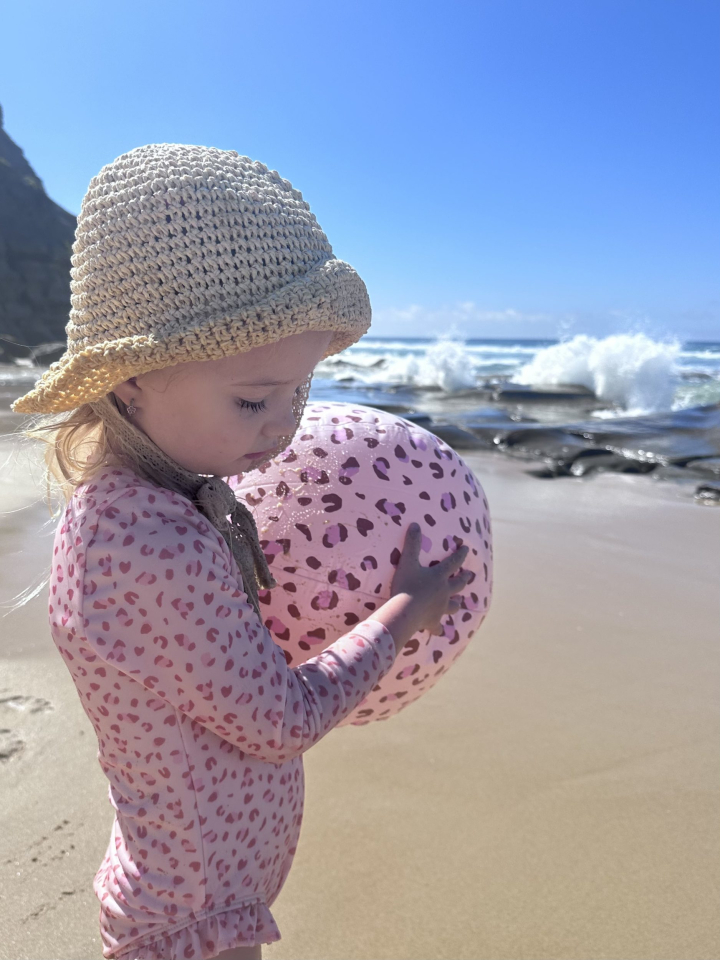 Kind speelt met roze bal op strand