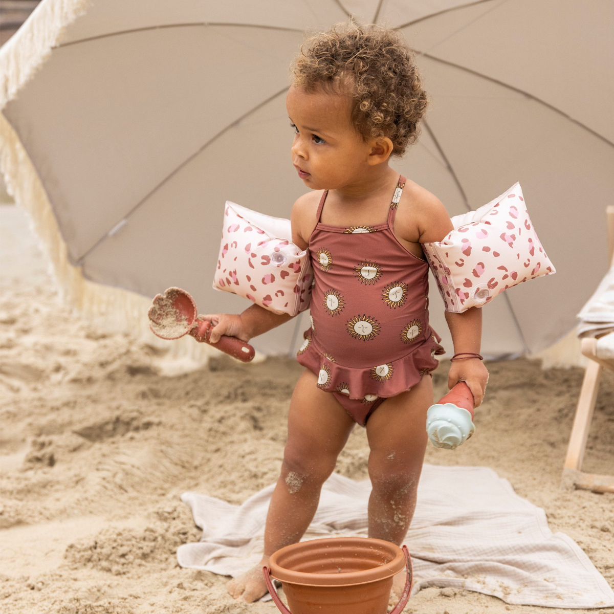 Peuter met speelgoed bij parasol op strand.