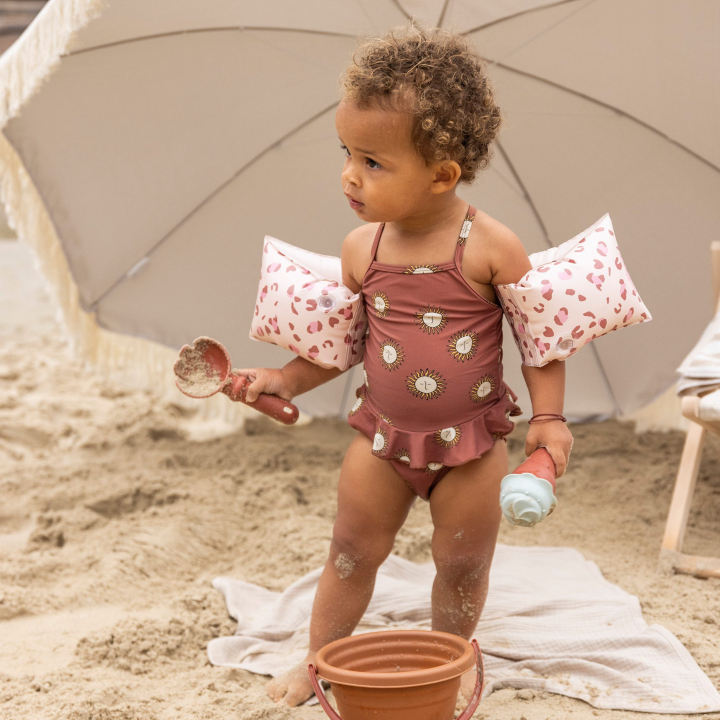 Peuter met speelgoed bij parasol op strand.