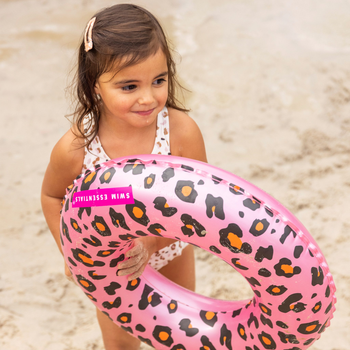 Kind met roze zwemband op strand.