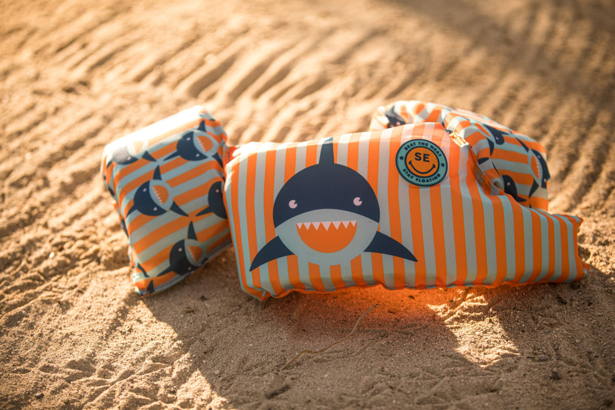Kinder zwembandjes met haaienprint op het zand.