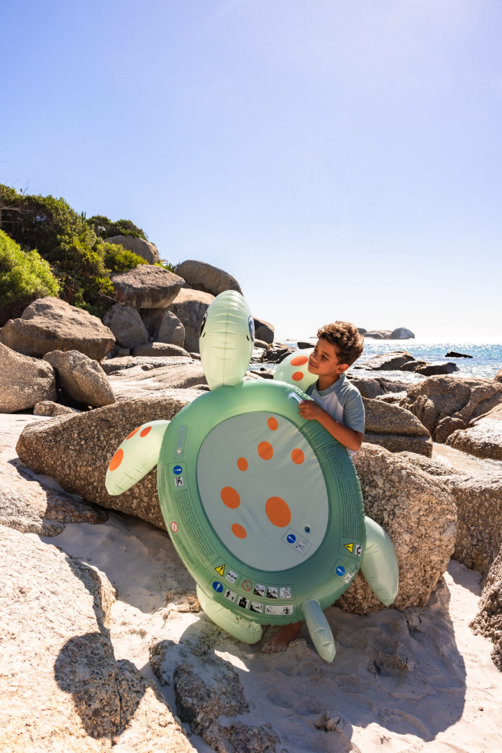 Kind met opblaasbare schildpad op strand.