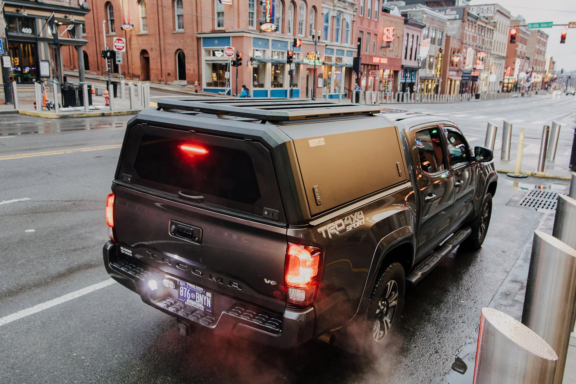 Stainless steel truck cap on a Toyota Tundra pickup truck parked on a city street with colorful brick buildings in the background.