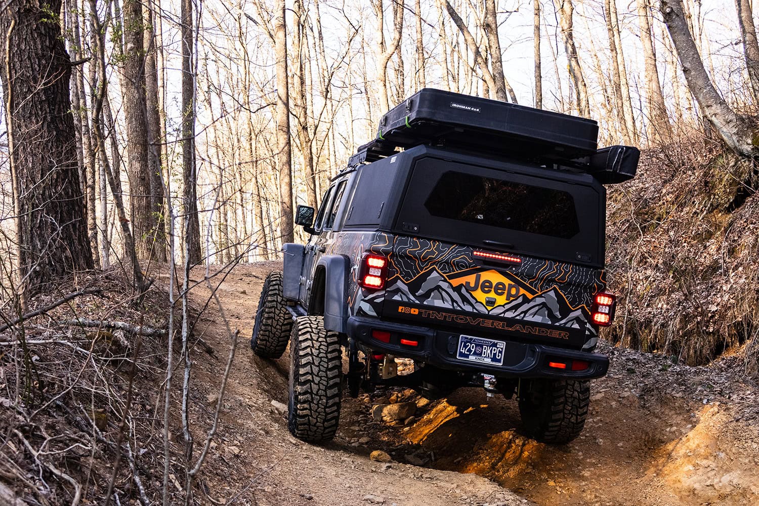 Durable stainless steel truck cap mounted on a Jeep overland vehicle in a rugged forest terrain.