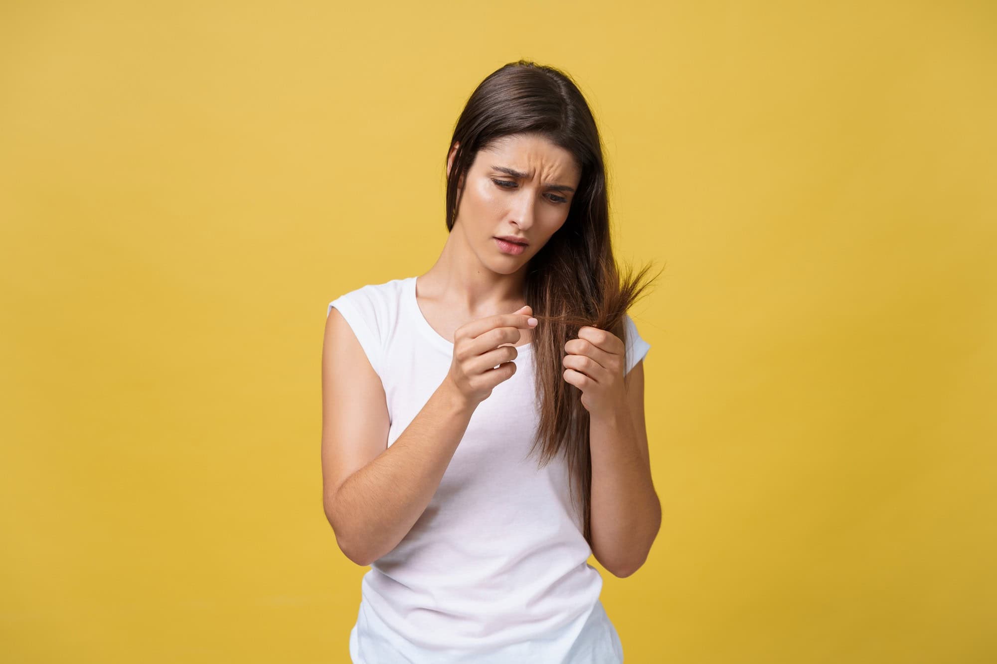 Hair thinning concern, woman examining hair loss on yellow background.