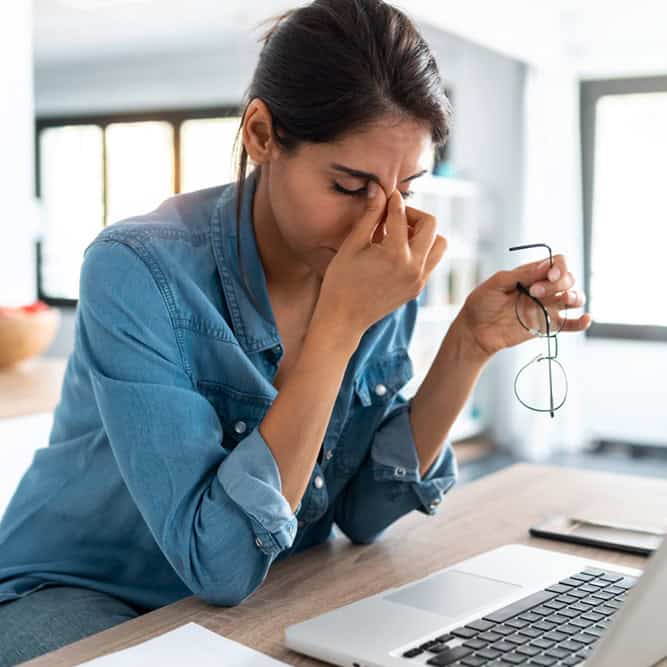 Stressed business woman working from home on laptop looking worried, tired and overwhelmed.