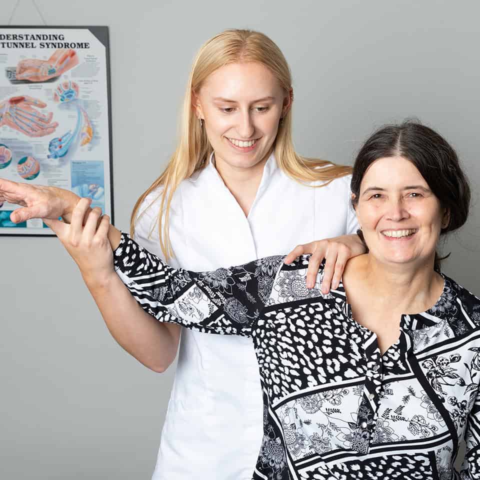 Georgina Joss, osteopath at Ashgrove Health Clinic, assisting a smiling patient with shoulder pain through gentle therapeutic movement.