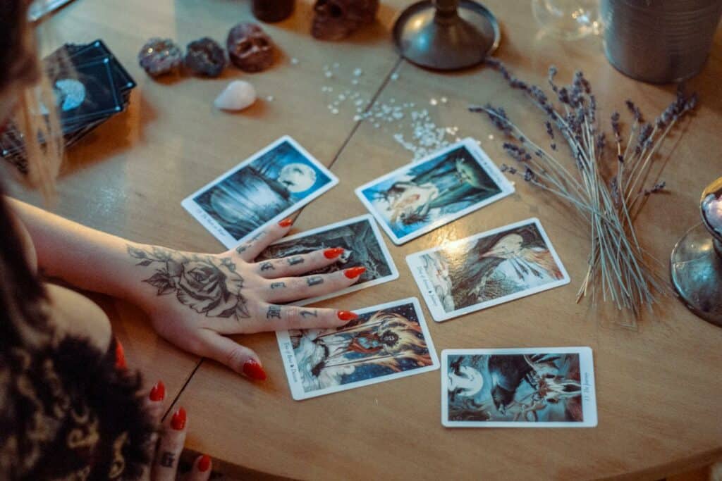 future, horoscope, A mystical setup featuring tarot card reading on a wooden table, with artistic tattoos and dried flowers.