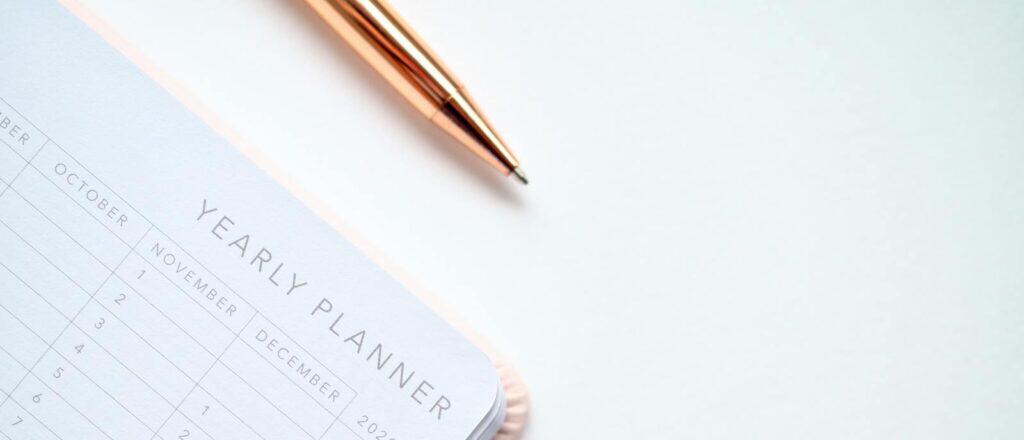 A stylish yearly planner open to a 2020 calendar page, accompanied by a golden pen on a clean white surface.