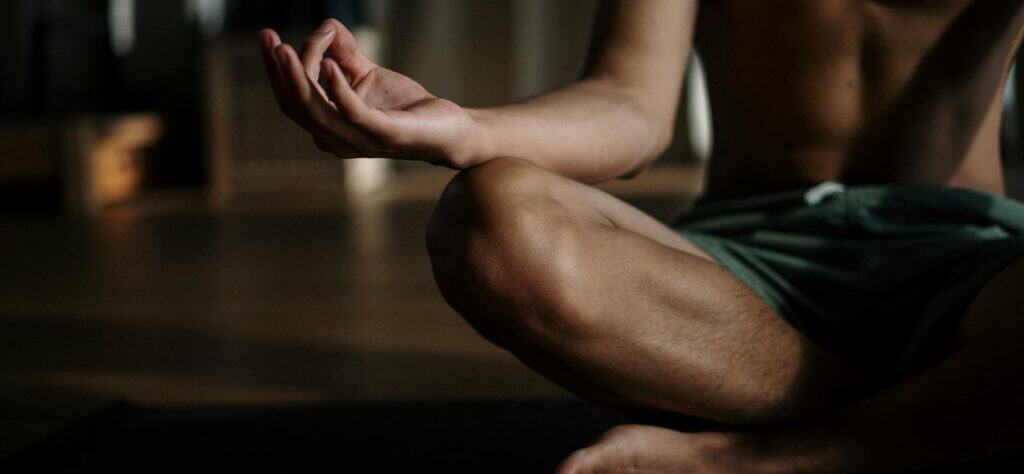 A shirtless man in a yoga studio meditating in the lotus position for relaxation and wellness.