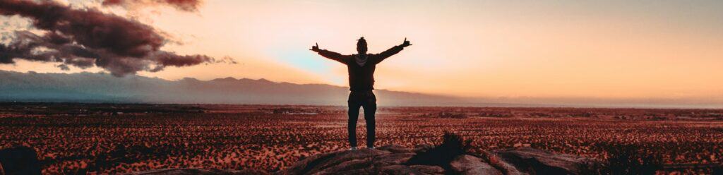 person standing on rock raising both hands