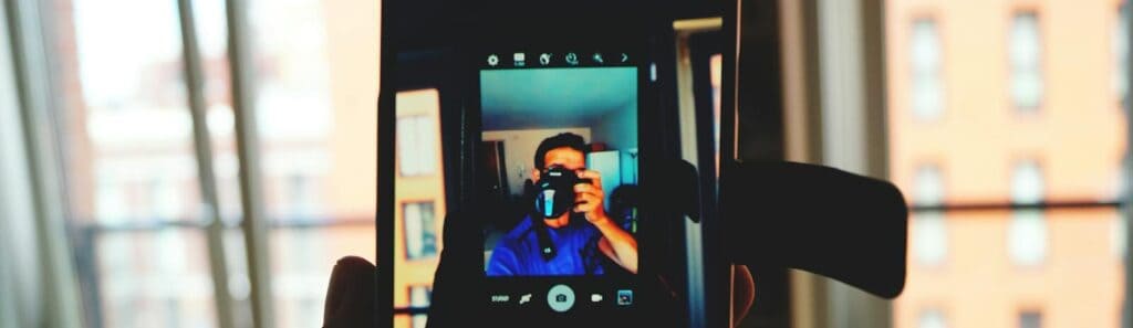 A man takes a smartphone selfie capturing his own reflection in an indoor urban setting.