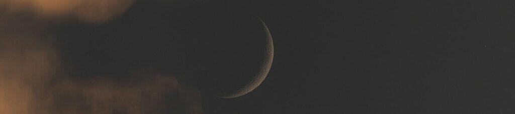 A crescent moon amidst dramatic clouds at night, creating an ethereal mood.