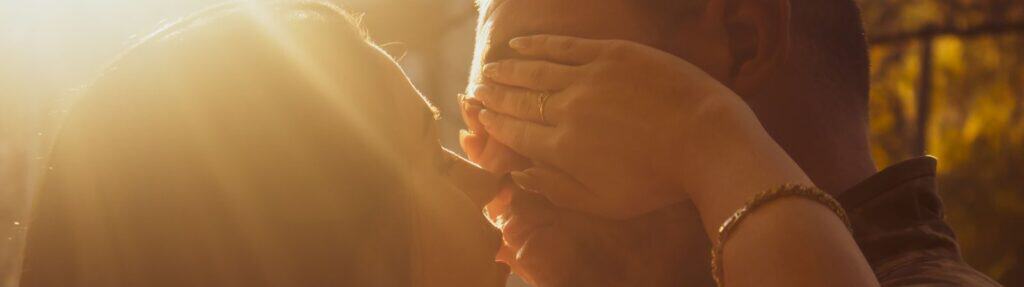 A couple shares an intimate kiss in warm, golden sunlight outdoors, evoking love and romance.