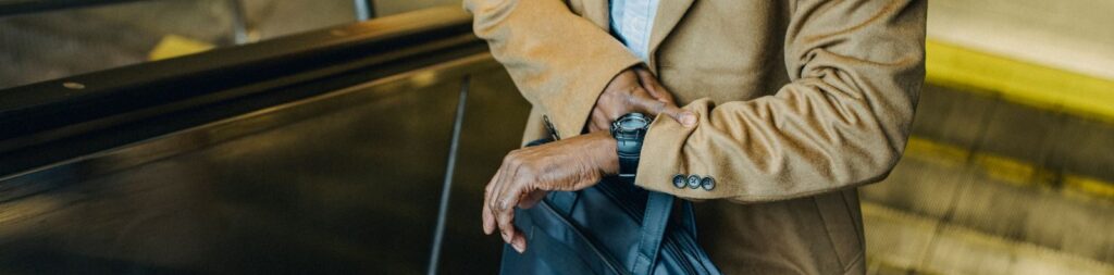 From above crop punctual African American businessman riding escalator and checking time on wristwatch while leaving metro station