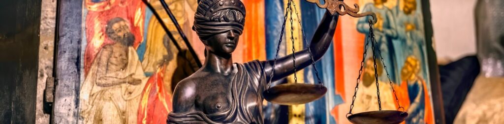 A blindfolded statue representing justice holding scales, set against an ornate background in Jerusalem.