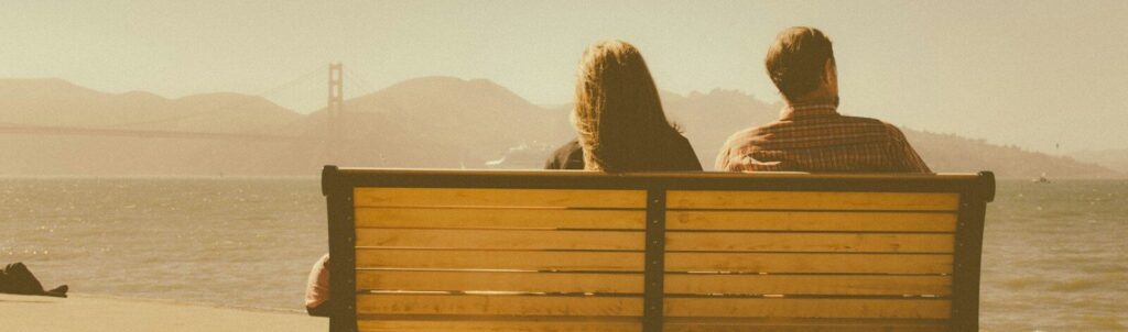 man and woman sitting on bench beside body of water