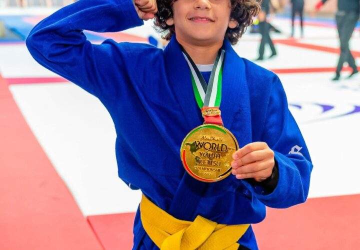 Young Atom Jiu Jitsu athlete Mohamed Syoud in a blue gi flexing and showing his gold medal at the World Youth Jiu Jitsu Championships