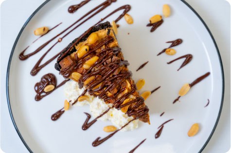 Delicious chocolate cake slice topped with nuts and drizzled with chocolate sauce.