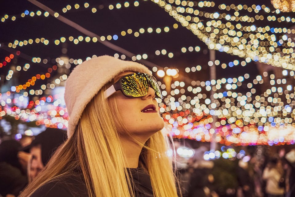 A young woman looks skyward and ponders smart home trends while wearing a pastel-pink hat under a night sky webbed with white lights.