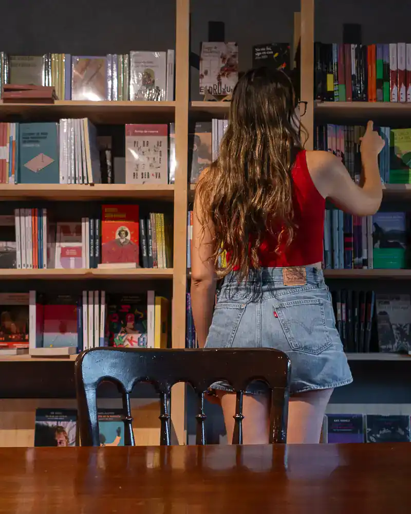 Young woman with long hair and glasses browsing books in a bookstore.