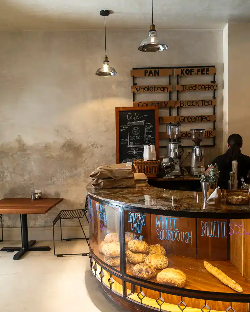 A cozy coffee shop with a curved glass display case filled with baked goods, a chalkboard menu, and rustic wooden wall decor.