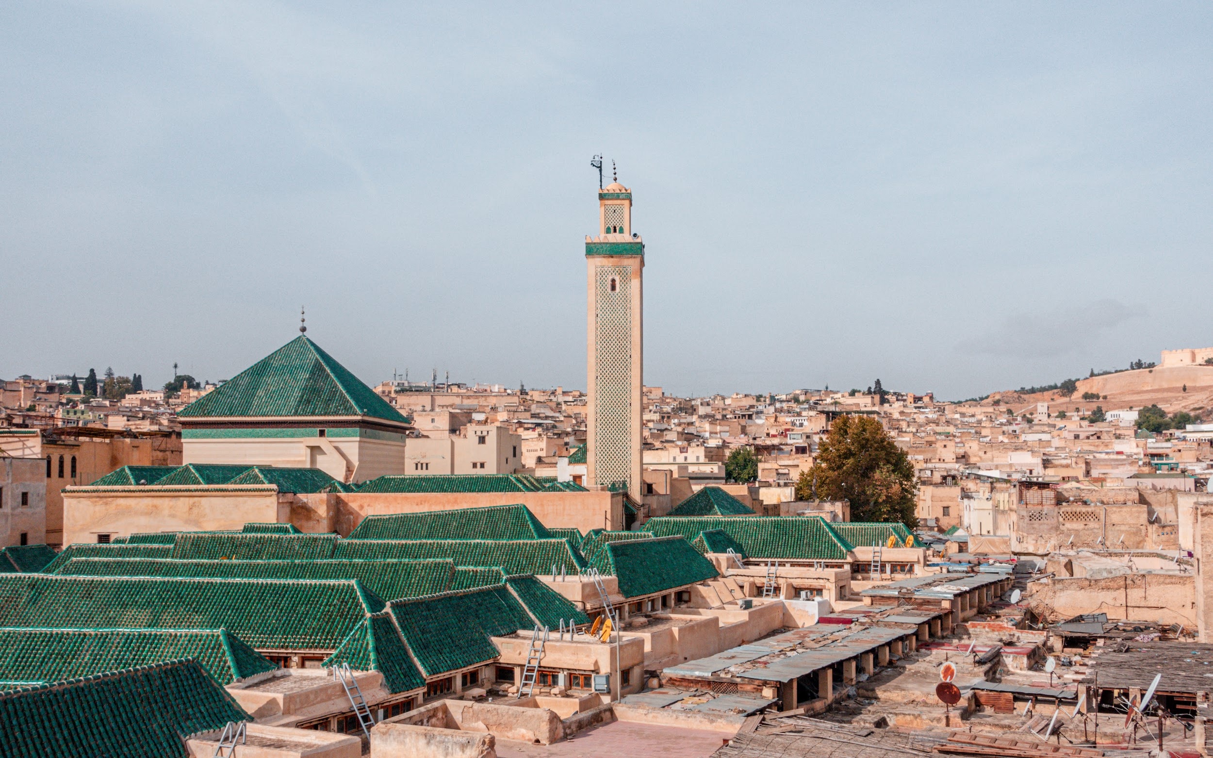 Colorful cityscape with a tall minaret and green-tiled roofs of buildings.