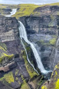 Smukt vandfald omgivet af grøn vegetation og klipper i Island, perfekt til naturoplevelser og eventyr.