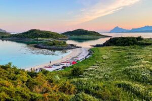 Smuk norsk fjord med grønne øer, sandstrand og teltpladser under solnedgangen.